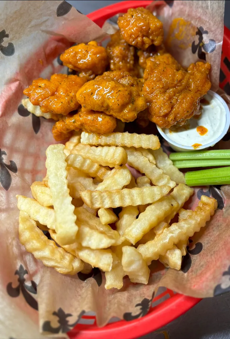 A red basket of buffalo-style chicken and crinkle-cut fries with a side of dipping sauce