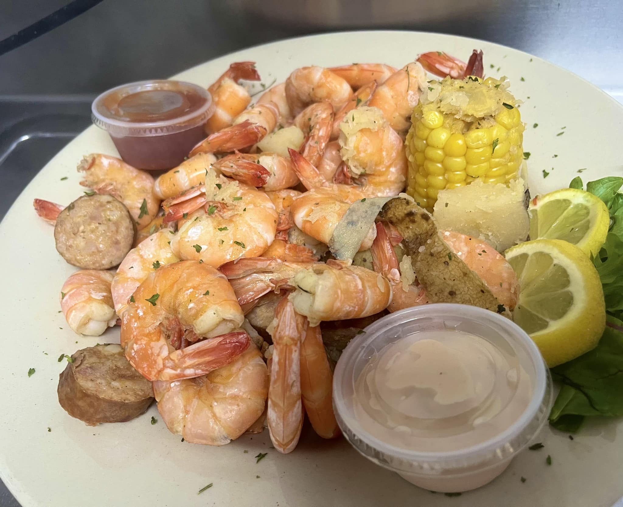 A boiled seafood plate of shrimp, corn on the cob, sliced sausage, lemon wedges, and dipping sauces