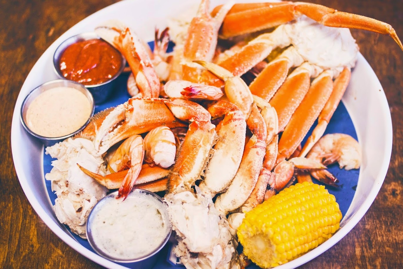 A white platter of crab legs, shrimp, and corn on the cob with three dipping sauces