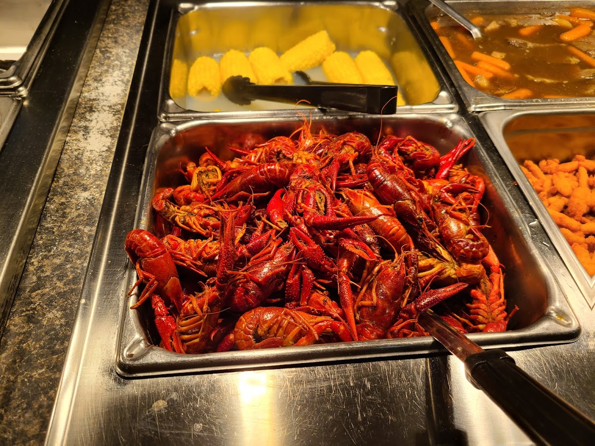 Steam table trays loaded with crawfish, corn and vegetables