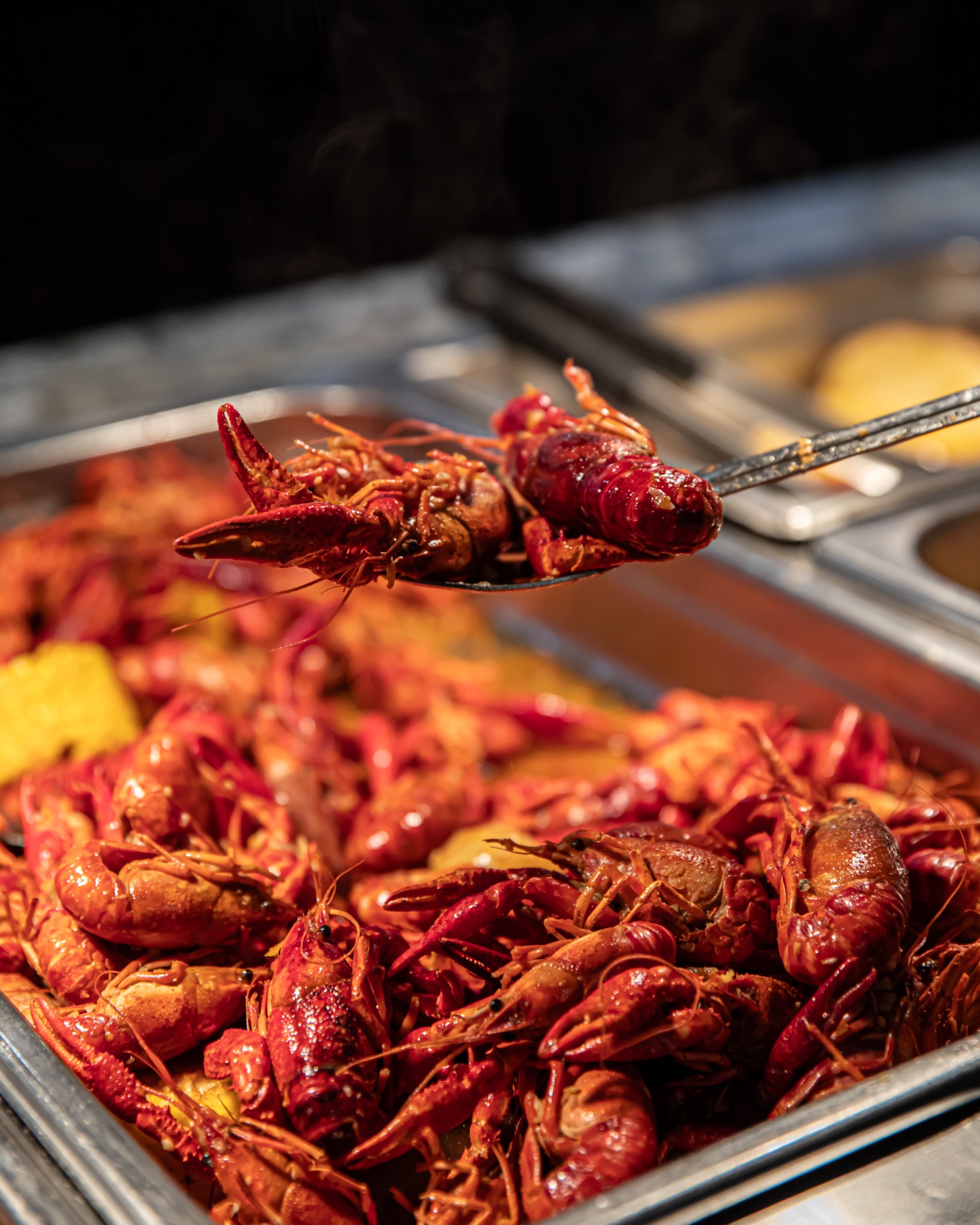 Steaming boiled crawfish being scooped from a metal tray with a serving utensil