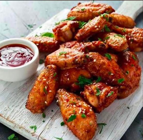Glazed chicken wings sprinkled with sesame seeds beside a bowl of red dipping sauce